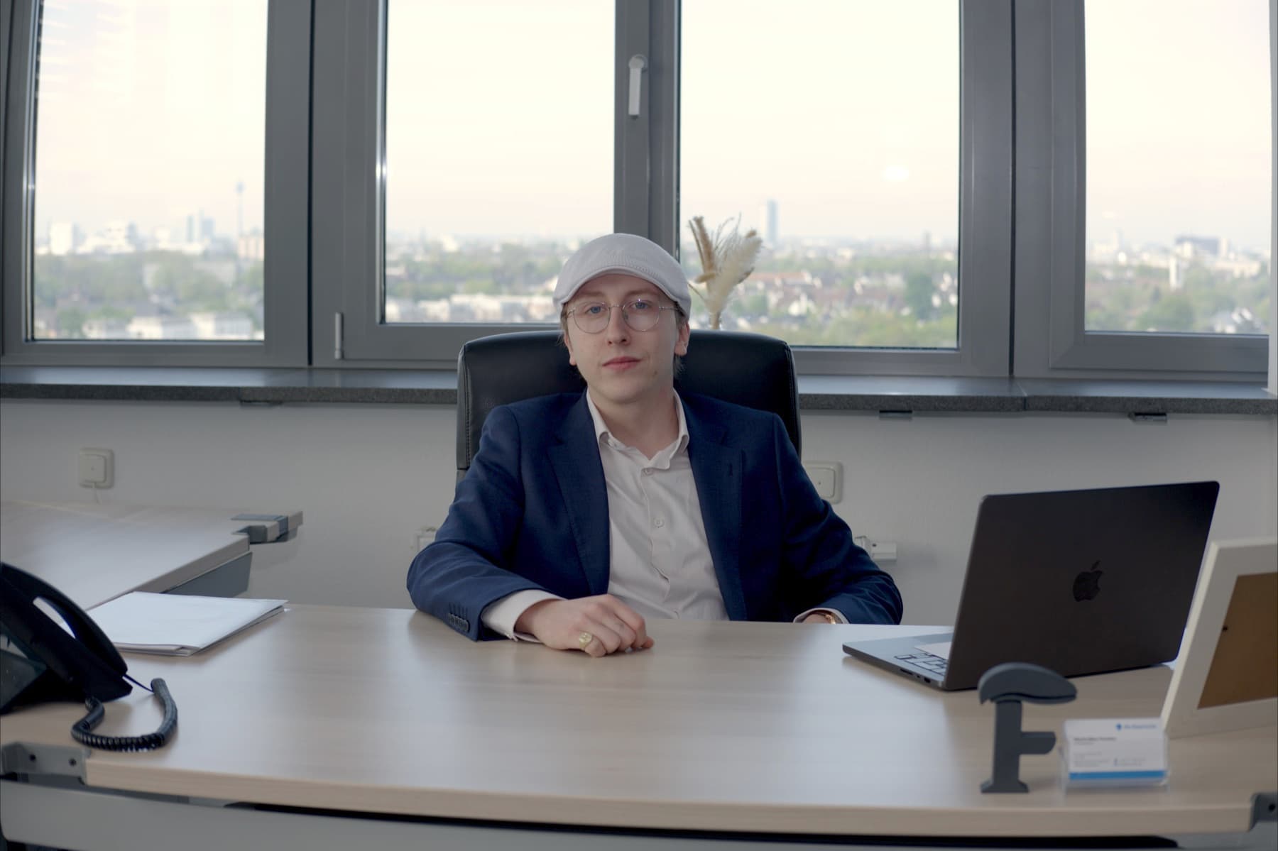 Maximilian Fanslau am Schreibtisch im Düsseldorfer Büro, mit Stadtpanorama im Hintergrund